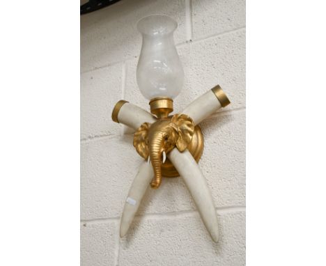 A gilt metal wall light with elephant's head and composite crossed tusks and glass shade, 55 cm overall 