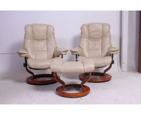 A pair of Norwegian designer Ekornes cream leather revolving Stressless reclining chairs with circular bases along with a mat