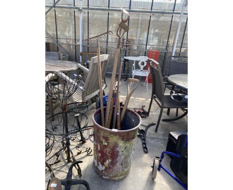 A VINTAGE METAL BUSTBIN WITH AN ASSORTMENT OF GARDEN TOOLS TO INCLUDE HOES, RAKE AND SHOVEL