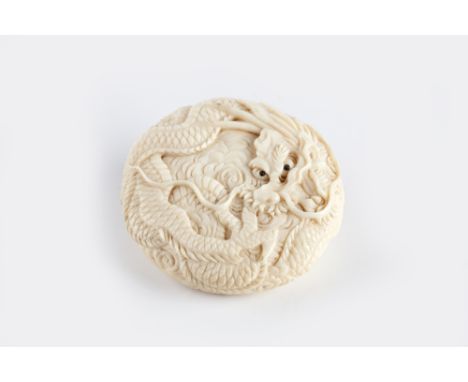 A Japanese ivory Manju netsuke Meiji period (1868-1912) carved depicting a dragon with a toggle, 5cm across 