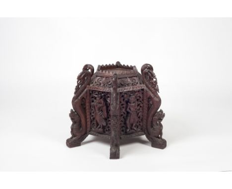 A Burmese hexagonal carved stand 19th Century with various deities to each panel and with dragon supports, 38cm high