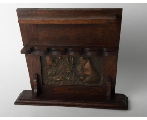 An Arts & Crafts wall hung wooden pipe rack inset bronzed panel depicting a man smoking, 14" wide