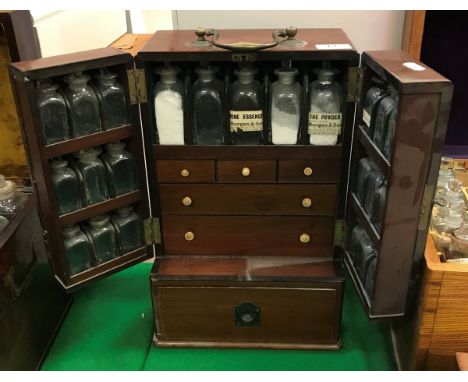 A Victorian mahogany apothecary's cabinet with brass swan-necked handle, the two doors each fitted with nine bottles, opening