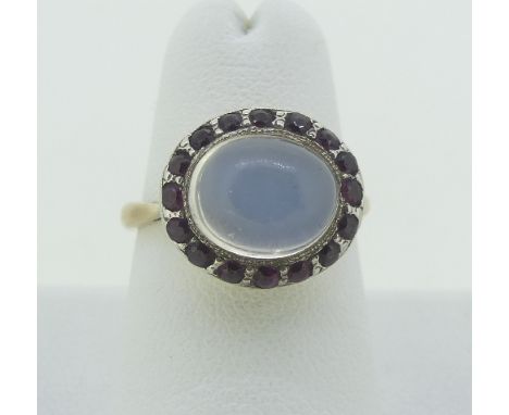 A moonstone and ruby Dress Ring, the central oval cabochon moonstone surrounded by sixteen small rubies, all mounted in white