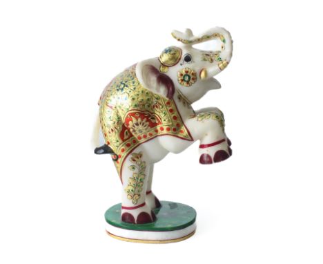 An Indian reconstituted marble figure of a rearing caparisoned elephant - the elephant with raised trunk, wearing an ornate s