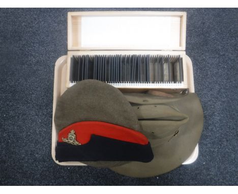 A pine slide box containing vintage glass negatives and three military hats bearing badges 