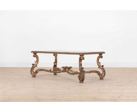 A carved giltwood coffee table, 20th century, Italian, the rectangular glass top raised on scrolling rococo supports united b