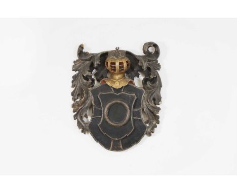 A carved and painted armorial crest, early 18th century, depicting a carved and giltwood helmet above a shield, flanked by ac