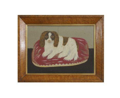 A Victorian folk art embroidery, mid to late 19th century, depicting a spaniel lying on a red cushion, worked in polychrome s