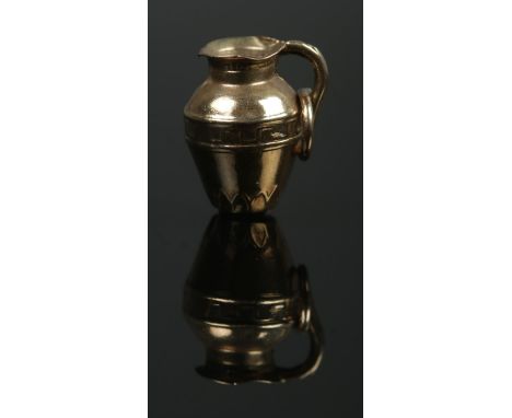 A 9ct Gold charm, formed as a water pitcher jug. Stamped to the side of the jug. Total weight: 0.8g.  Minor dents to the jug.