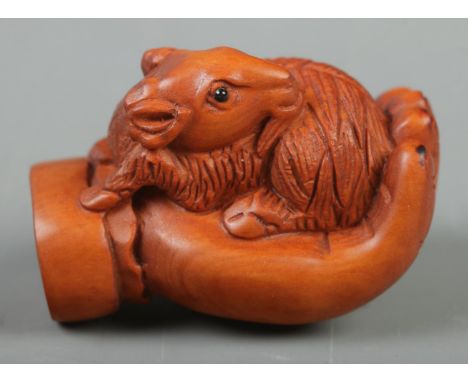 A Japanese carved Netsuke in the form of a goat on hand  