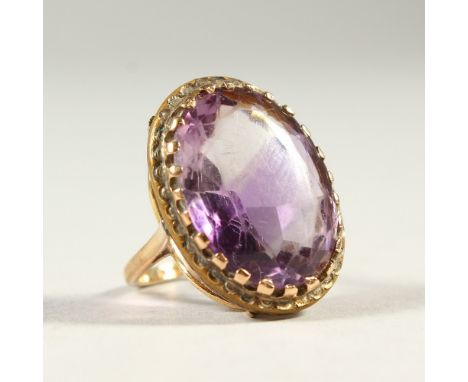 A GOLD RING SET WITH A LARGE AMETHYST COLOURED STONE.