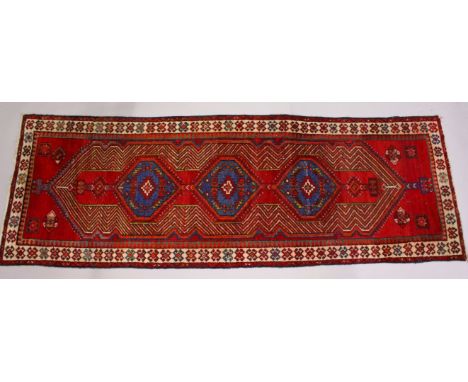 A PERSIAN LONG CARPET / RUNNER, bright red ground with three blue ground motifs in a stylized border. 325cms x 110cms.