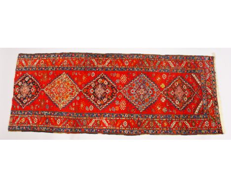 A PERSIAN LONG CARPET, bright red ground with five large medallions (reduced in length). 294cms x 116cms.