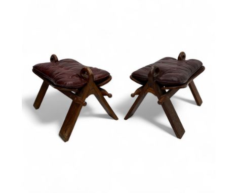 Pair of early 20th century Anglo-Indian camel saddle stools, with deep buttoned red leather upholstered seats and horn-shaped
