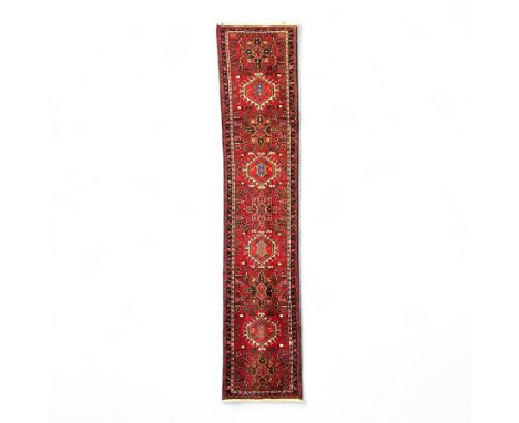 Persian wool runner, red ground with repeating hooked medallions and stylised geometric motifs in navy, ivory, and ochre, wit