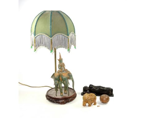 Thai metal group with a figure sitting on an elephant with 3 heads beneath a silk and glass bead tasselled shade, on a carved