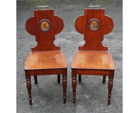 A pair of early 19th century mahogany armorial crested hall chairs the lobed tablet form backs centred with brass carrying ha