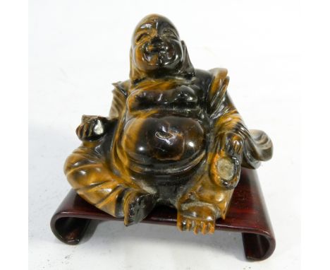A Chinese carved tigers eye recumbent Buddha on associated scroll shaped hardwood stand  7cms tall