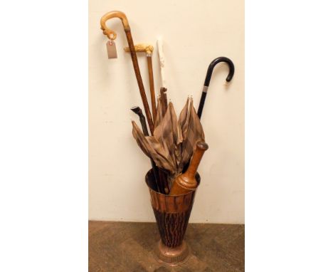 A copper stick stand with various walking sticks and umbrella 