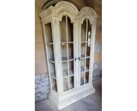 An impressive cantered vitrine, the shaped double arched oversailing cornice above two shaped field panelled glazed doors enc