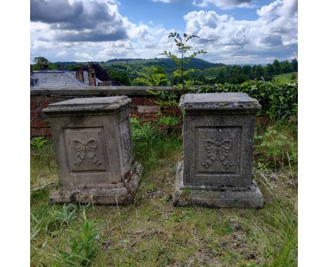 A pair of reconstituted gritstone garden plinths, Neo Classical ribbon tied bow decoration to each side panel, 61cm H x 44cm 