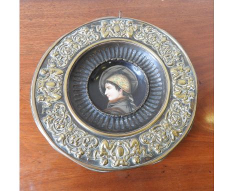ORNATE EMBOSSED BRASS WALL PLAQUE WITH CERAMIC PORTRAIT PANEL INSIDE, 29cm dia, the border embossed with cherubic decoration 