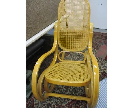 A modern light wood, cane seated rocking chair with two mixed cushions 