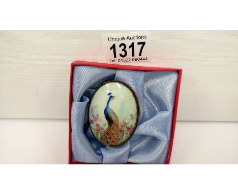 An oval enamel brooch depicting a peacock amongst flowers by the Royal Worcester painter C Gresley (signed), in 9ct gold moun