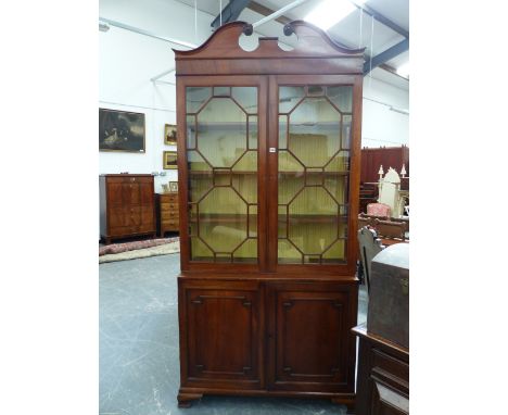 A GEORGIAN CARVED MAHOGANY BOOKCASE CABINET, SCROLL BROKEN PEDIMENT ABOVE GLAZED DOORS, PANELLED DOOR LOWER SECTION, BRACKET 