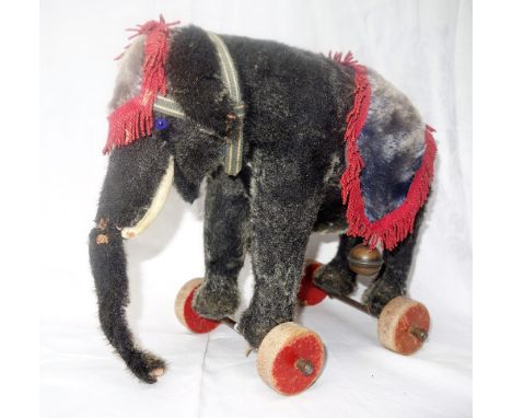 STEIFF; A DARK PLUSH PULL-ALONG ELEPHANT on red wooden wheels with blue velvet cover and red trimming, 27 cm high x 33 cm lon