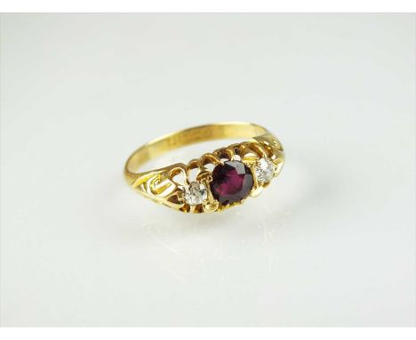 An 18ct gold three stone untested ruby and diamond ring, designed as a central round mixed cut ruby flanked to each side by a