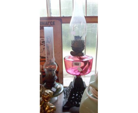 A Victorian double burner oil lamp with cranberry reservoir, cast iron base and glass chimney - sold with a sit in oil lamp r
