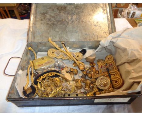 An old japanned box containing a large quantity of military button, cap badges, braiding, epaulettes, etc.