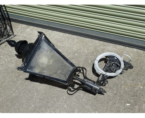 A black painted wrought iron wall mounted street lamp with four glazed panels, height 110cm, depth 76cm. 