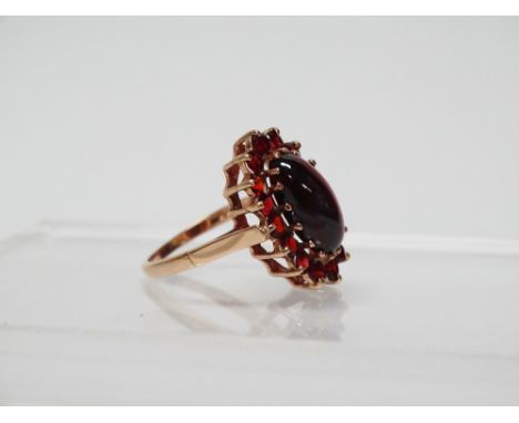 9ct gold and garnet ring - A 9ct gold ring set a large oval cabochon garnet surrounded by sixteen brilliant cut garnets, size