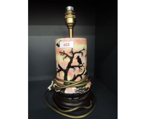 A modern Cobridge stoneware table lamp having black tree and silhoutette pattern on flame sky ground