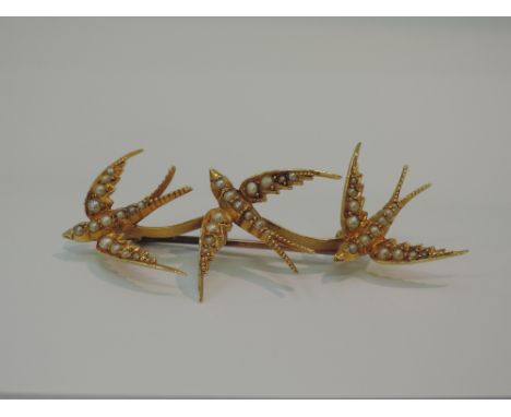 An Edwardian style yellow metal brooch modelled as a trio of swallows in flight with seed pearl decoration, no marks but test