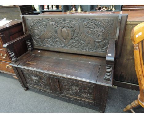 A mid 20th century dark oak monks bench in the Jacobean style having carved armorial crest and lions mask decoration