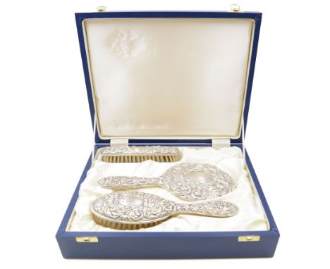 Modern silver mounted three piece dressing table set, comprising hand mirror, clothes brush and hair brush, all with embossed