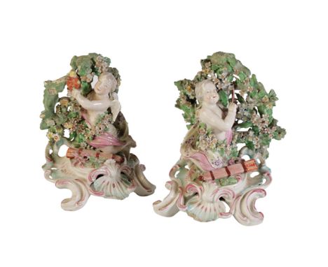 PAIR OF CHELSEA DERBY CHERUB CANDLEHOLDERS, circa 1765, modelled with a bocage background, on pierced rococo bases, 18cm, a F
