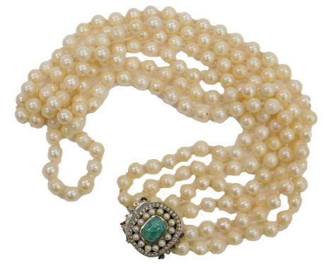 A cultured pearl three strand necklace, on a white metal snap clasp, set with a blue agate, in a surround of simulated pearls