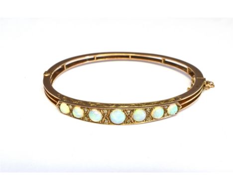 AN EDWARDIAN GOLD, OPAL AND DIAMOND HINGED BANGLE the front designed as a row of seven slightly graduated round-cabochon whit