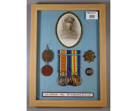 Framed and glazed WWI medal duo together with photograph, dog tags, cap badge, and enamelled Comrades of the Great War pin ba