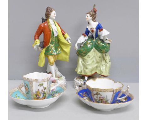 A pair of early 20th Century German porcelain figures and two Dresden cups and saucers, (fingers on gentleman a/f)