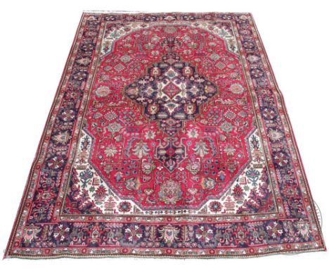 A Persian Tabriz wool carpet, worked with a geometric medallion design against a red ground, 300cm x 205cm 