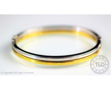 A 9ct bi-colour gold bangle, designed in half white and half yellow gold, clasp with safety catch, weight 9gms 
