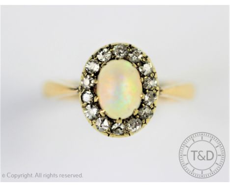 An opal and diamond oval cluster ring, the central oval opal within a diamond set surround, tapering shoulders and plain yell