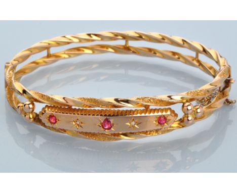A Victorian style ruby, diamond and 9ct. yellow gold bangle, the central plaque set with three facet cut rubies and two senai