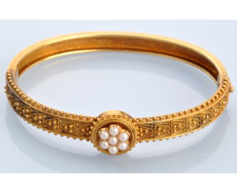 A yellow metal and half pearl bangle, of Etruscan design, the central half pearl cluster within bead and filigree work, plain